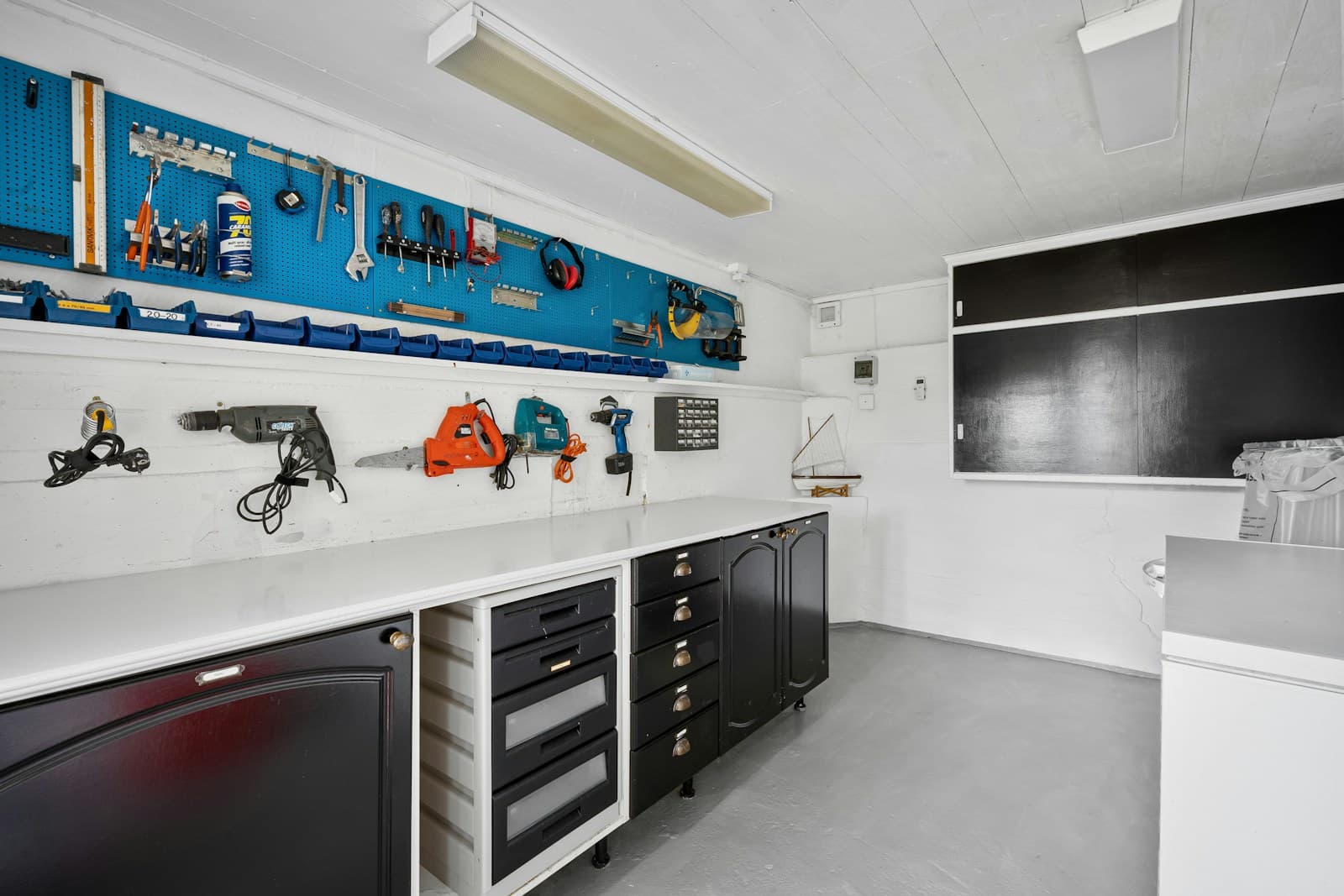 Bright garage workbench with black cabinets, a white counter and organized tools